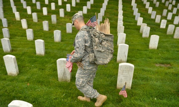 A soldier places flags at grave sites in Arlington National Cemetery.